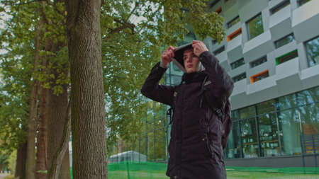 Portrait of a hipster young man putting on a hood while looking at the camera. Close up view of millennial boy in dark hoodie smiling standing on the street. People emotion conceptの写真素材