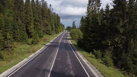 Aerial low air flight over mountain perfect asphalt highway road and meadow at sunny summer morning....