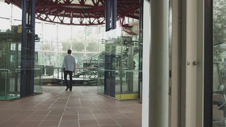 A stylishly dressed man walks down a glass corridor in a modern office. Shooting from the back of the hands. Confident man on his way to work ready to achieve his goals.の写真素材