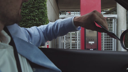 young male businessman in nice suit and glasses paying for parking by bank card with car leaving his...