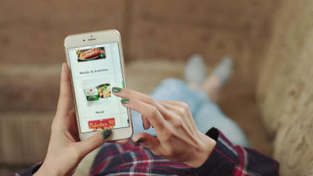 Woman at Home Lying on Couch in Living Room Using Smartphone Buys in Internet Shop. Woman Orders Ice Cream Home In An Online Store Using a Smartphone. Female Selects Ice Cream in Grocery Online Store.のeditorial素材