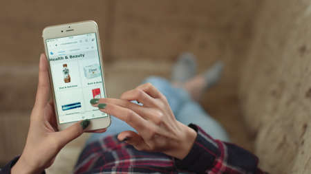 Woman at Home Lying on Couch in Living Room Using Smartphone Buys in Internet Shop. Woman Orders Health Beauty Home In An Online Store Using a Smartphone. Female Selects Health Beauty in Grocery Online Store. POVの写真素材