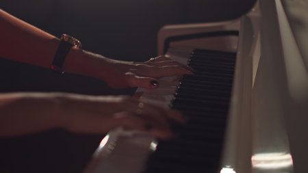 A female young hands playing piano in black manicure and accessories. Classical music pattern. Girl...