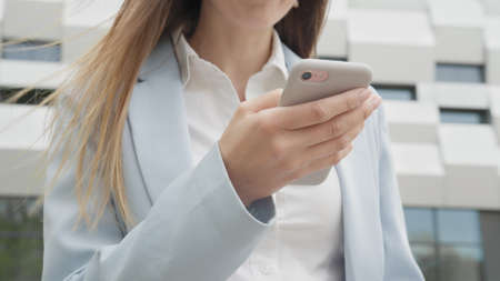 Appealing young elegant woman using social media application on smartphone text messages receive news smiling outdoor. People portraits. Technology. Closeup joyful girl reading good news on phone.の写真素材