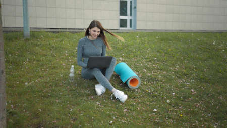 Happy woman, sitting laptop outdoor. Smiling fit girl typing on laptop computer at city background. Person working on laptop outside. Attractive girl, corporate startup office employee working outdoorの写真素材