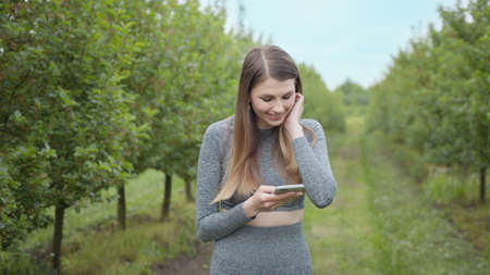 Happy woman typing by mobile phone outdoors. Cheerful girl with smartphone in park on a background. Smiling lady holding cellphone in hands outside. Athletic fitness girl holding a phone in her hands.の写真素材