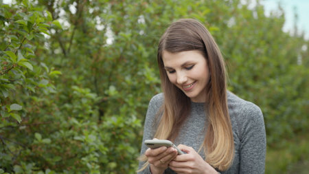 Happy young woman use smartphone standing in park sun outdoor health hand girl tree sport fitness summer nature internet technology female runner exercise phone workout mobile cell phoneの写真素材