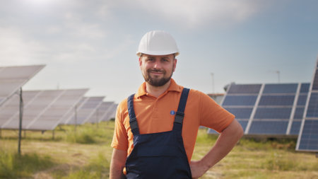 Portrait ecology worker in hard hat standing at solar panel field. Industrial people. Portrait of male engineer in hard helmet turning head and looking to camera. Concept of solar station developmentの写真素材