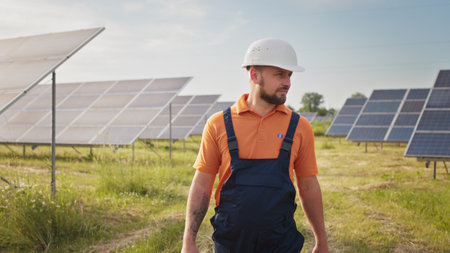 Industrial man engineer in uniform walking through solar panel field for examination. Ecological...