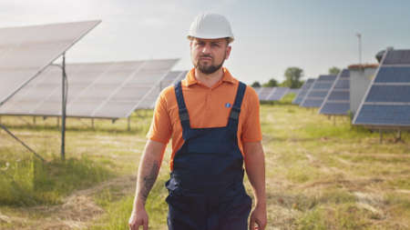 Industrial man engineer in uniform walking through solar panel field for examination. Ecological construction. Solar power station, Green energy concept. Solar station development and energyの写真素材