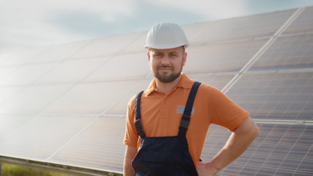 Portrait of ecological expert industrial worker in uniform standing by solar panels installation. Construction of solar station. Workman. Clean energy production. Green energy. Ecological solar farm.の写真素材