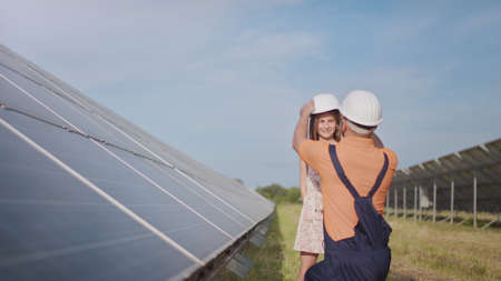 An young father is engineer explains to his little daughter an operation and performance of photovoltaic solar panels at sunset. Concept:renewable energy, technology, electricity,green,future, familyの写真素材