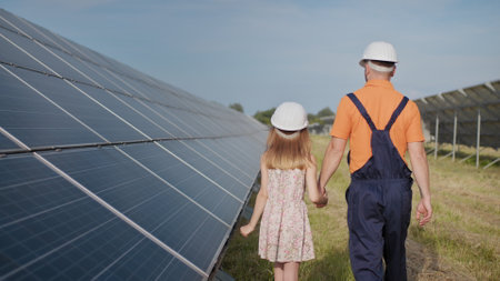 A father working in a solar power plant tells his daughter about his work, shows green energy, solar panels. Shooting at a solar power plant. Preservation of our planet, global warmingの写真素材