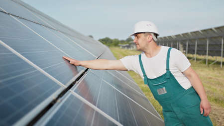 Portrait of proud worker industrial engineer in uniform standing on field with large solar batteries. Ecological farm. Solar power station. People. Sustainable energy. Solar power field. Ecology.の写真素材