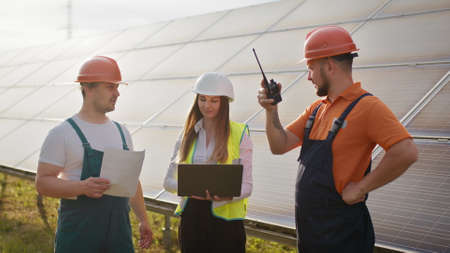 Three solar energy specialists walking at a solar power facility. Professional engineers discuss innovative project. Business team. Clean energy. Professional engineers discuss innovative projectの写真素材