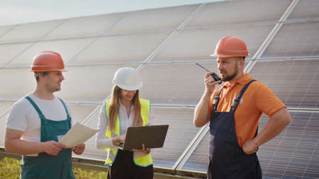 Team of industrial colleagues using tablet monitoring rows of photovoltaic solar panels at sunset. Business cooperation. Solar park. Alternative energy concept. Clean energyの写真素材