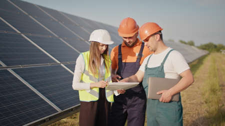 Engineers use drawings on the solar farm in special uniform standing look around discuss the installation of sunny batteries electricity environmental slow motion. Meeting with the investorの写真素材