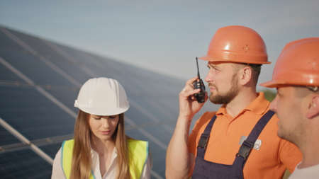 Ecological station. Alternative energy. Engineers use drawings on the solar farm in special uniform standing look around discuss the installation of sunny batteries. Solar panels fieldの写真素材