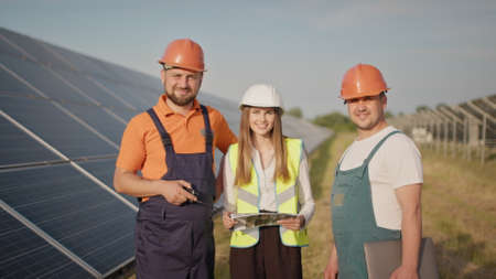 Ecological station. Alternative energy. Engineers use drawings on the solar farm in special uniform standing look around discuss the installation of sunny batteries. Solar panels fieldの写真素材