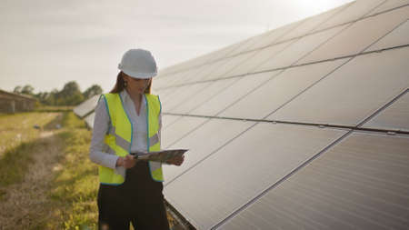 Female ecological engineer uses project documents and files and collects efficient information about solar panels. Photovoltaic solar farm. Green energy. Environment. Concept of green energyの写真素材