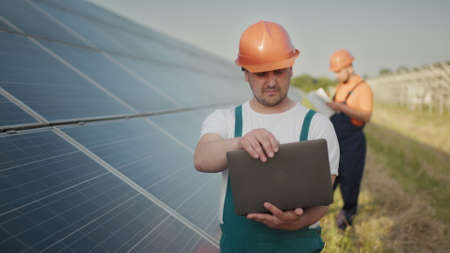 Engineer standing with Solar cell panels looking monitor of the Electric power value made from the solar cell. Man holding laptop in her hands standing on field with solar panels. Solar energyの写真素材