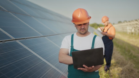 Engineer standing with Solar cell panels looking monitor of the Electric power value made from the solar cell. Man holding laptop in her hands standing on field with solar panels. Solar energyの写真素材