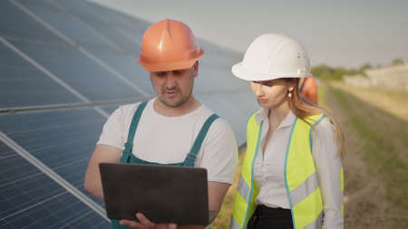 Technician and investor walking in Solar cell Farm through field of solar panels checking the panels at solar energy installation. Employees of power plant and talking about scheme of solar panels.の写真素材
