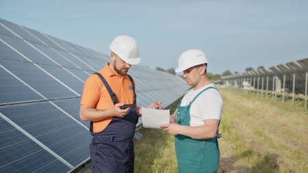 Chief engineer and specialists learning the report of investment for solar plant construction. Business team. Negotiation. Clean energy. Industry. Engineers installing new sunny batteries.の写真素材