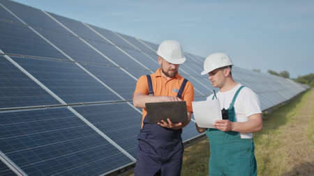 Energy specialist using digital tablet reading information to check the efficiency of solar panel construction. Green energy jobs. Technology. Two solar power plant workers are recording dataの写真素材