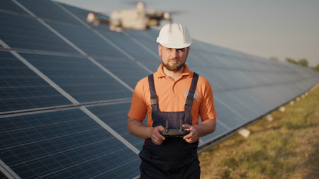 Industrial expert wearing helmet and controlling drone in photovoltaic solar power plant. Solar...