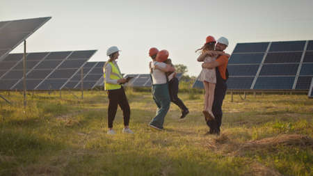 Two small children run to their parents who are at work. A solar power plant employee with children at work smiling at the camera. Three solar energy specialists at a solar power facility.の写真素材