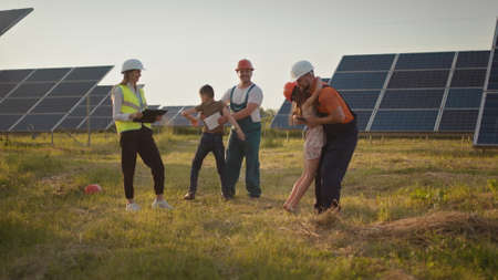 Two small children run to their parents who are at work. A solar power plant employee with children at work smiling at the camera. Three solar energy specialists at a solar power facility.の写真素材