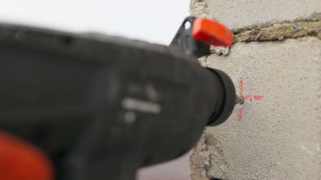 SLOW MOTION,: Builder working uses an electric drill to mount a wall panel. Man drills hole using perforator. Male hands held electric drill with drill bit rotating and making cement dust from wall.の写真素材