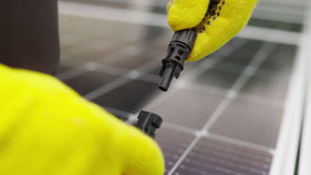 Close up of connecting electric cable to solar panels. Connection and installation of solar panels. Connection to the solar energy network. An electrician in gloves connects the cableの写真素材