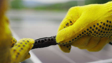 Solar Station Equipment. Connecting wires of solar panels at a solar farm. Engineers connect electrical system outdoors on a background of solar panels. Worker in protective gloves connects wireの写真素材