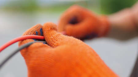 An electrician worker holds a red and black high-voltage electric cable, checks the quality of the cables. Connecting electrical cables. Close up of male hands in protective gloves holding cableの写真素材