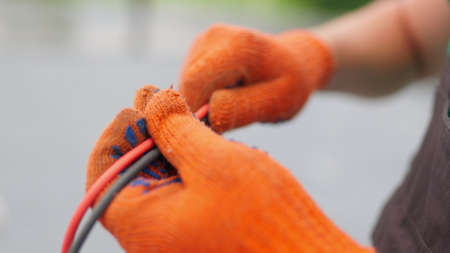 An electrician worker holds a red and black high-voltage electric cable, checks the quality of the cables. Connecting electrical cables. Close up of male hands in protective gloves holding cableの写真素材