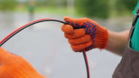 An electrician worker holds a red and black high-voltage electric cable, checks the quality of the cables. Connecting electrical cables. Close up of male hands in protective gloves holding cableの写真素材