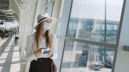 Beautiful business woman at the airport, using the phone to send text messages, standing by the window in the corporate office building, looking at the camera. The girl is holding tickets and a passport.の写真素材