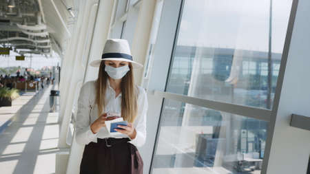 Beautiful business woman at the airport, using the phone to send text messages, standing by the window in the corporate office building, checking messages. The girl is holding tickets and a passportの写真素材