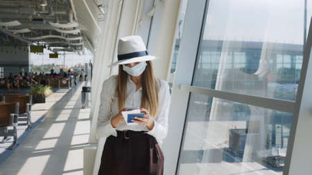 Beautiful business woman at the airport, using the phone to send text messages, standing by the window in the corporate office building, looking at the camera. The girl is holding tickets and a passport.の写真素材