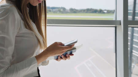 Close up of business womans hands using smartphone send text messages at the gate of the airport terminal while waiting for the flight, mobile phone checks emails, business trips, mobile phone.の写真素材