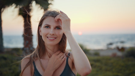 Adorable caucasian woman in green sport bra standing on sea beach with palms and smiling on camera. Active female person relaxing during intense workout among exotic nature.の写真素材