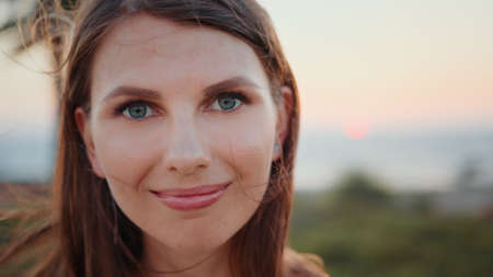 Close up portrait of stunning young woman with long brown hair and blue eyes posing on ocean beach. Sporty female relaxation during evening training on fresh air.の写真素材