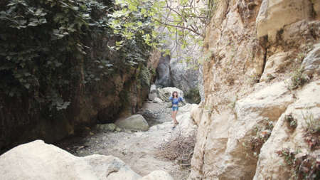 Back view of young woman in blue blouse, denim shorts and white hat walking along canyon of high rocks during warm summer day. Adventure of young female person. Travelling concept.の写真素材