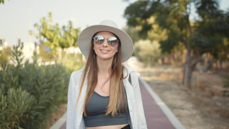 Happy young woman in summer clothes, hat and sunglasses walking with backpack outdoors. Palm trees around. Concept of people, vacation and tourism.の写真素材