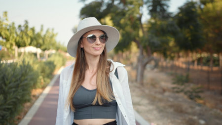 Portrait of a beautiful young girl in glasses. Happy young woman in summer clothes, hat and sunglasses walking with backpack outdoors. Palm trees around. Concept of people, vacation and tourism.の写真素材