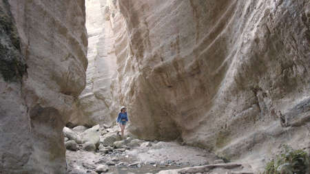 Happy young woman wearing blue blouse, denim shorts and white hat standing among high rocks, holding hands up and turning around. Enjoyment, freedom and travelling concept. Happy woman in summer.の写真素材