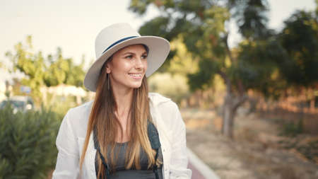 Happy young woman using modern digital camera for taking photos while walking. Female tourist in summer hat and clothes saving memories from trip.の写真素材