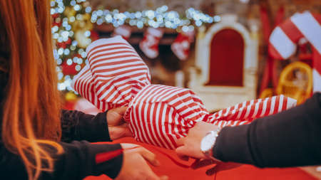Close up of female hands making a big Christmas decoration in the form of candy in a Christmas store or house. In the background, the fireplace is decorated with Christmas lights and socks.の写真素材